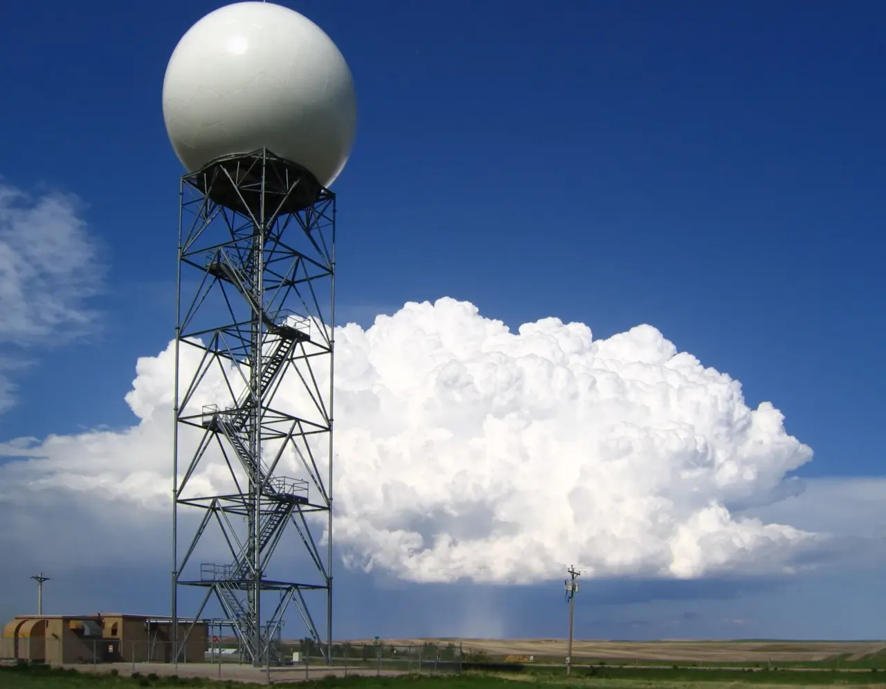 Açık alanda beyaz küresel bir radar kubbesi; arkasında koyu fırtına bulutları ve yağmur perdesi.