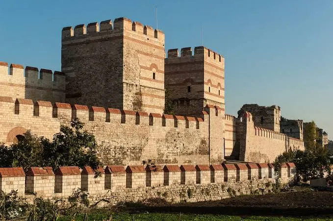 Konstantinopolis'in taş ve tuğla kuşaklı çok katmanlı kara surları ve burçları, altın ışıkta.