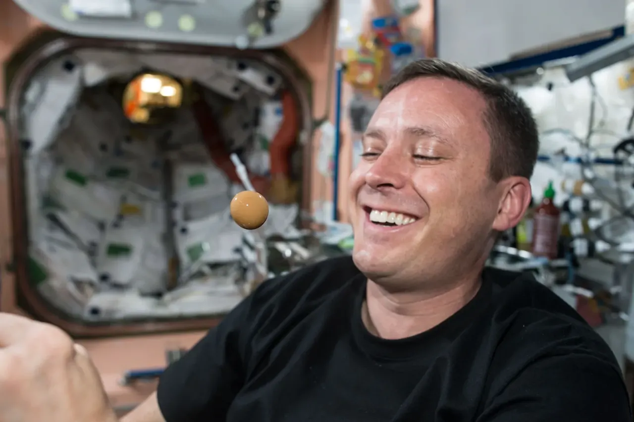Uzay istasyonunun içinde havada asılı duran küresel bir su damlası; arkada bir astronot.