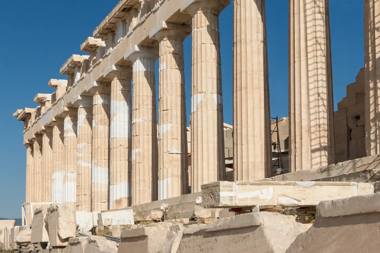 Parthenon’un batı kolonadı: yivli mermer sütunlar sıralanmış, üstünde kırık alınlık, arkada mavi gökyüzü.