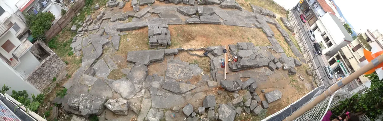Şehir içinde, alçak duvarlarla çevrili arkeolojik alanda sıra sıra kırık sütun kaideleri ve temel taşları.